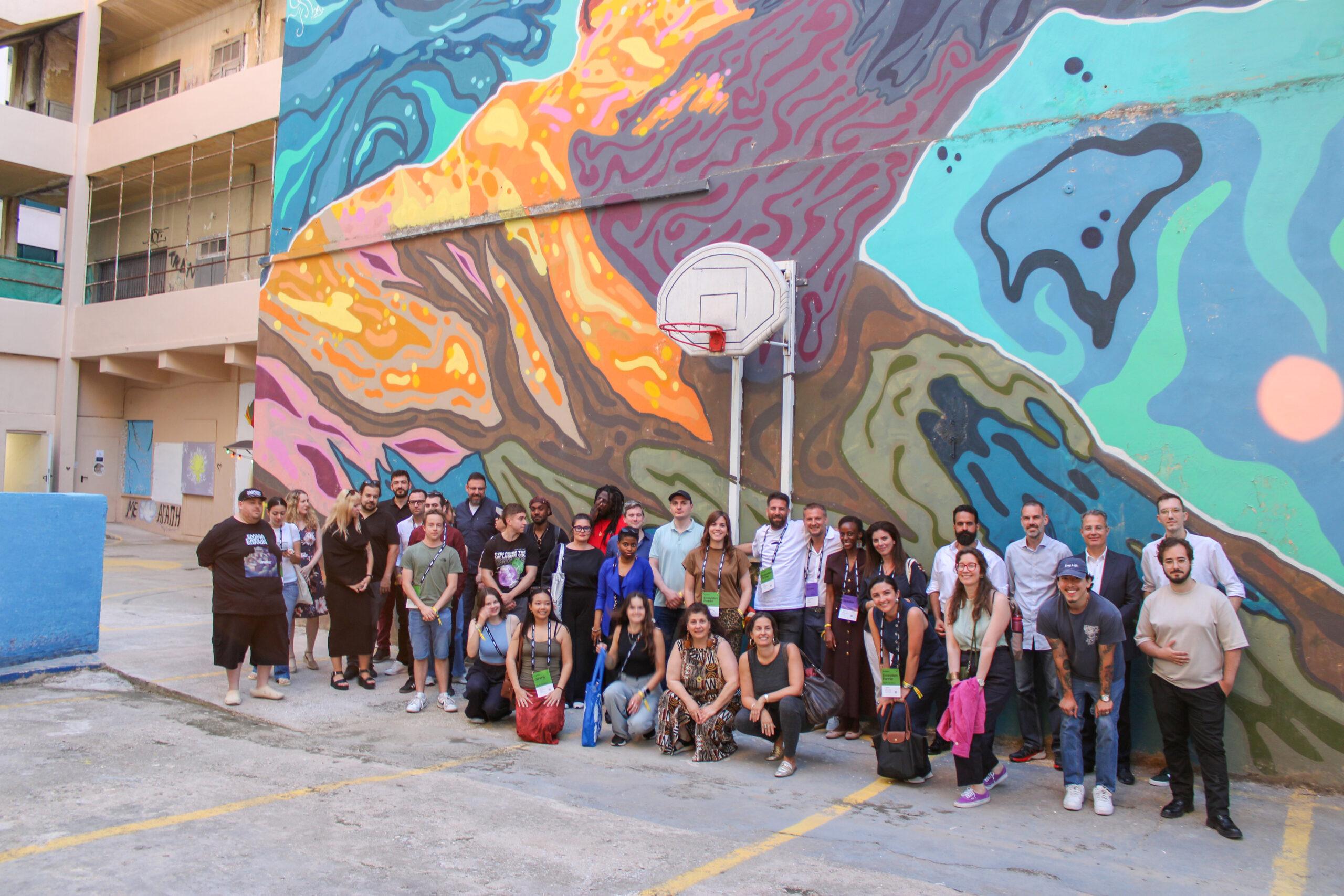 Group of people posing in front of colorful wall mural during an event.