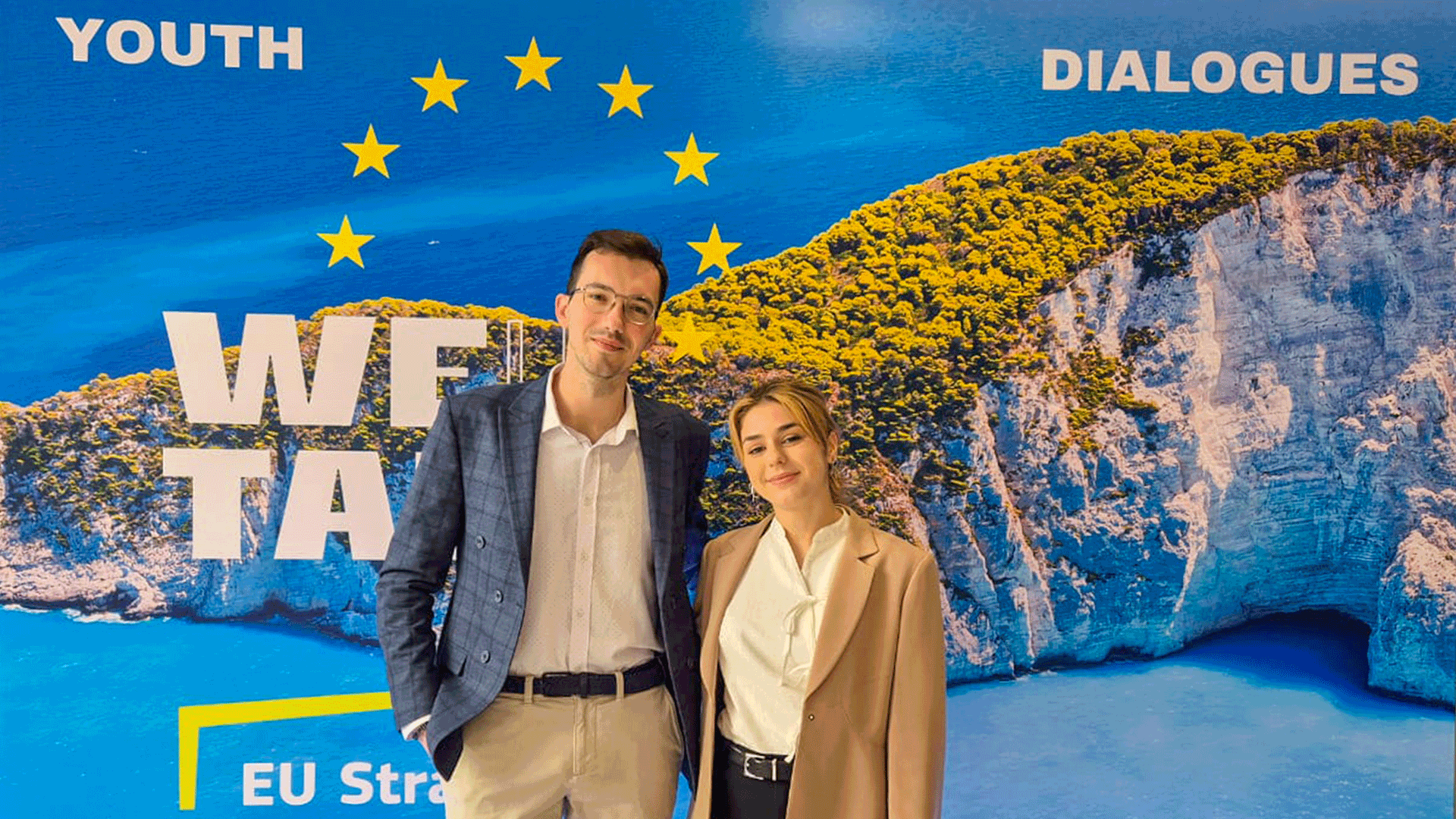 Stefanos Stagakis and Vasili Kasioni from Youthmakers Hub posing in front of WEUtalk banner during the outh Policy Dialogue on Sustainable Tourism in Athens, Greece