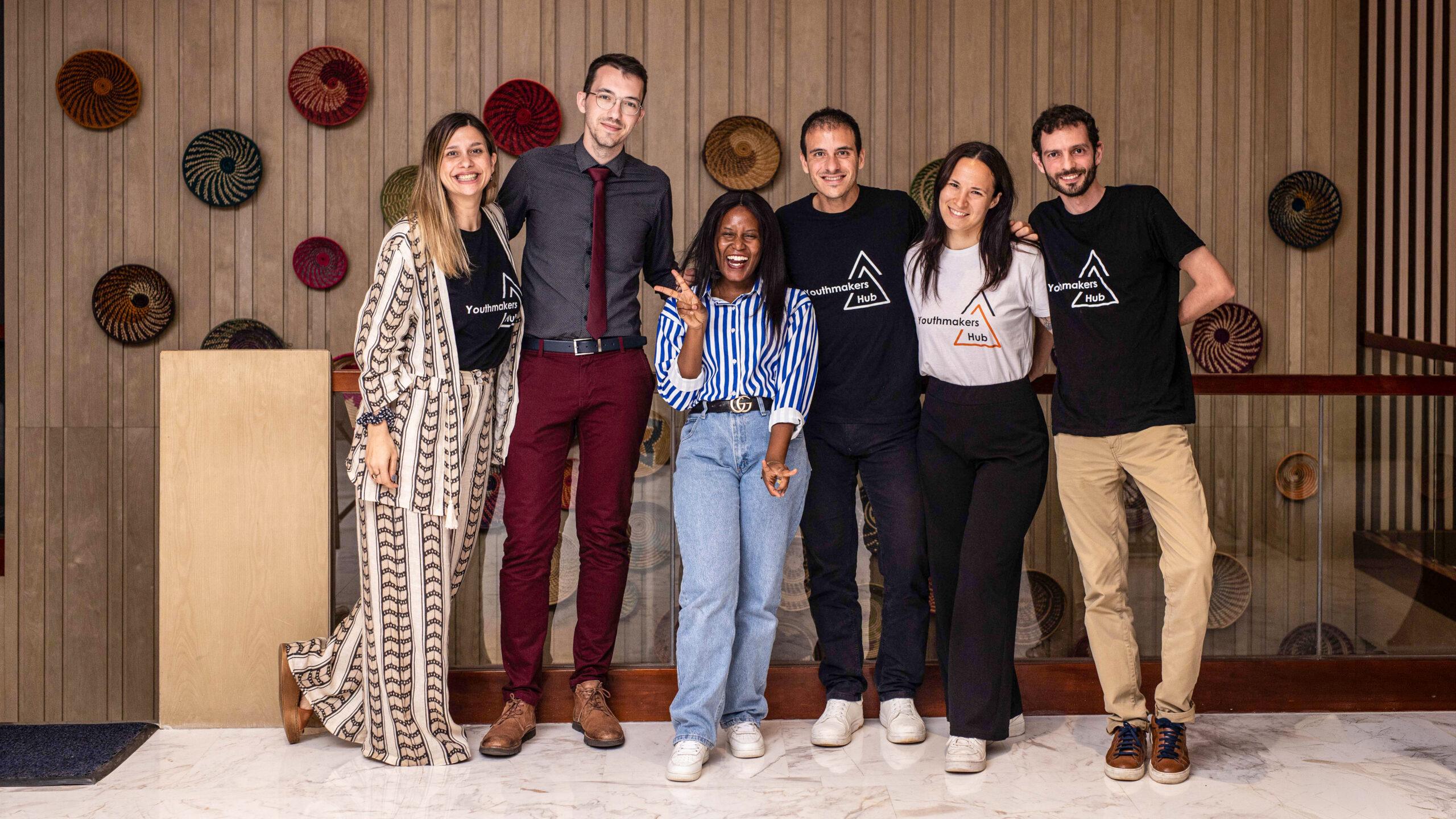 Group of six people posing indoors. 4 of them wearing Youthmakers Hub merch t-shirts.